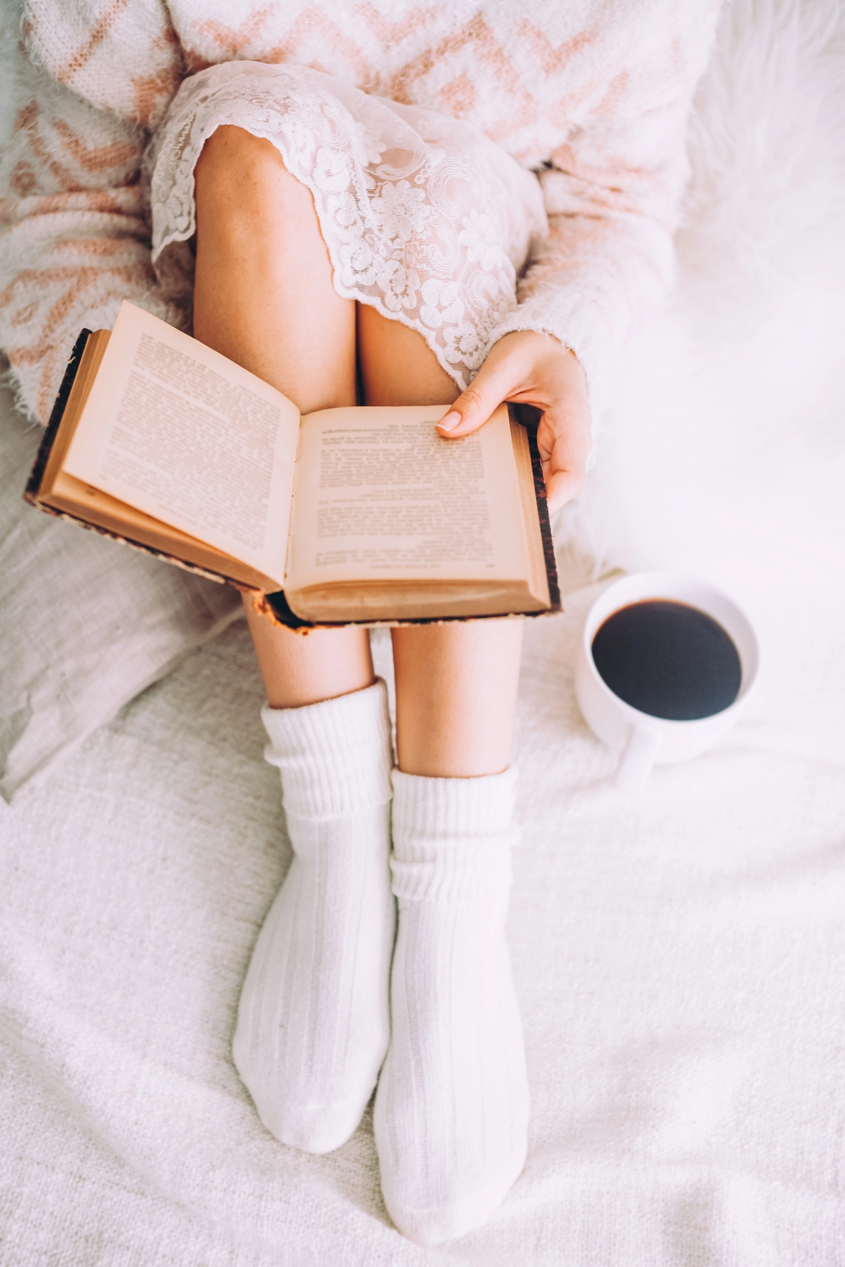 Woman wearing lace skirt and white socks reading a book with a cup of coffee.