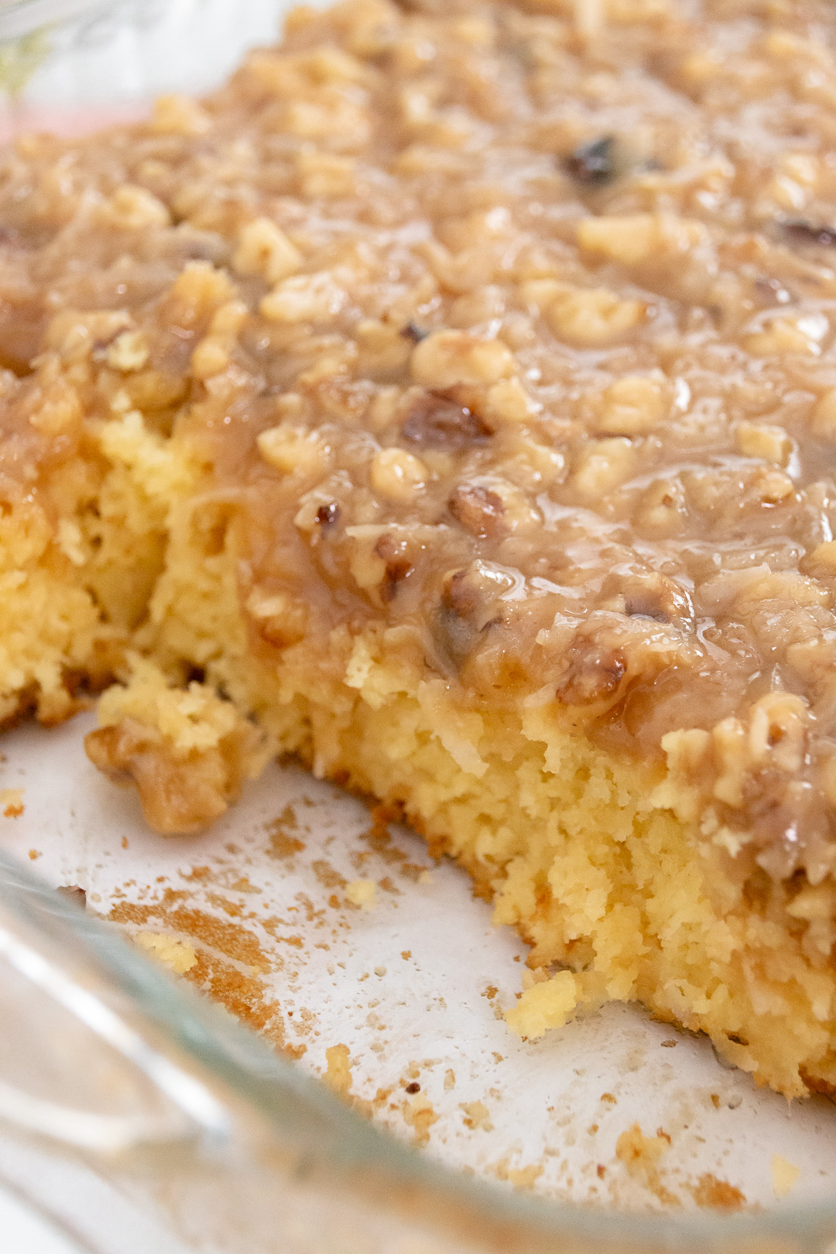 Tornado cake in a glass baking dish with a gooey coconut and nut topping; one corner piece has been served.