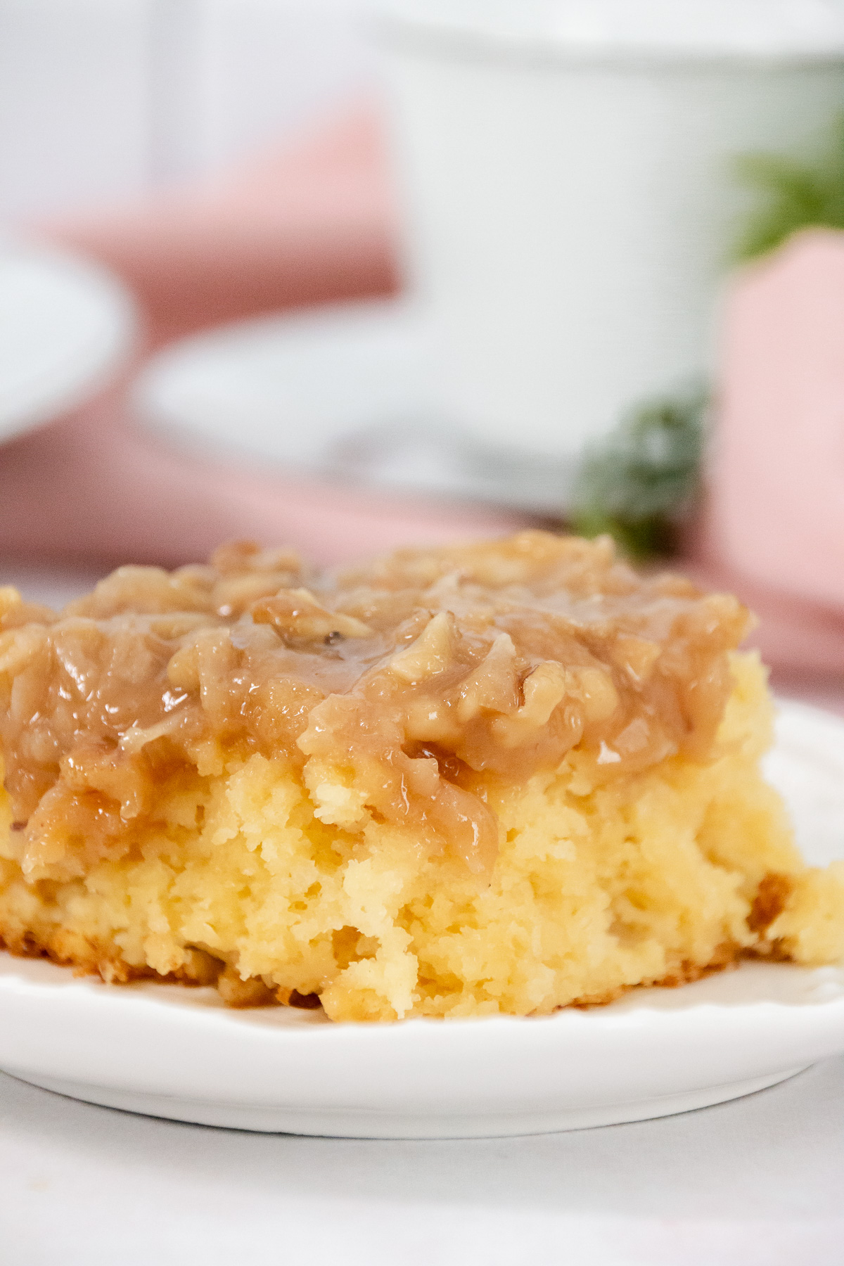 Close-up of a moist slice of tornado cake with gooey coconut-nut topping on a white plate.