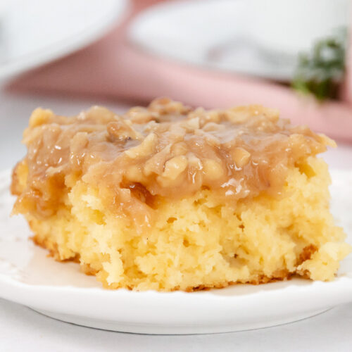 Single slice of tornado cake with golden yellow crumb and gooey coconut-nut topping on a white decorative plate.