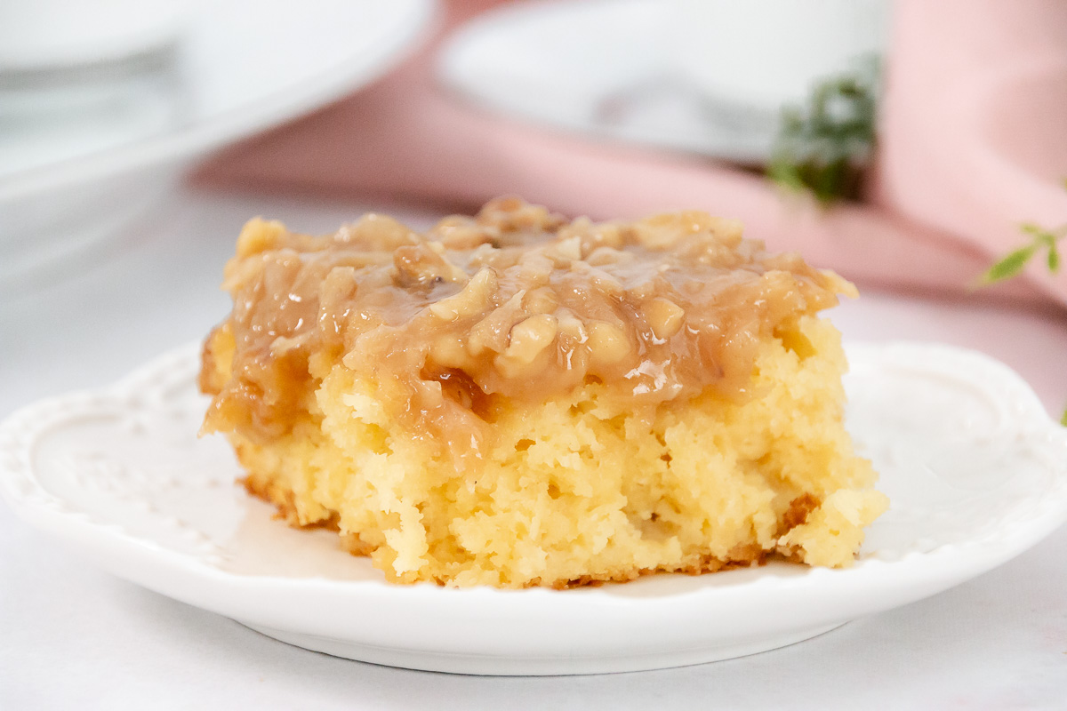 Single slice of tornado cake with golden yellow crumb and gooey coconut-nut topping on a white decorative plate.