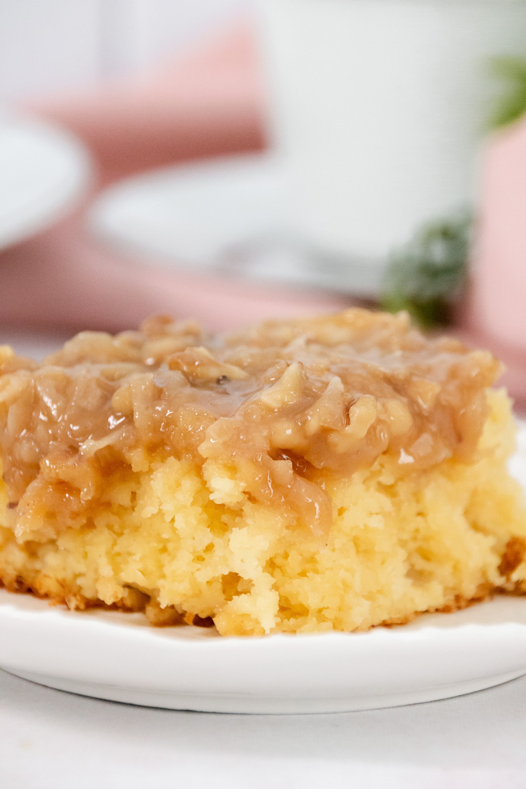 Close-up of a slice of tornado cake with caramel coconut-nut topping on a white plate.