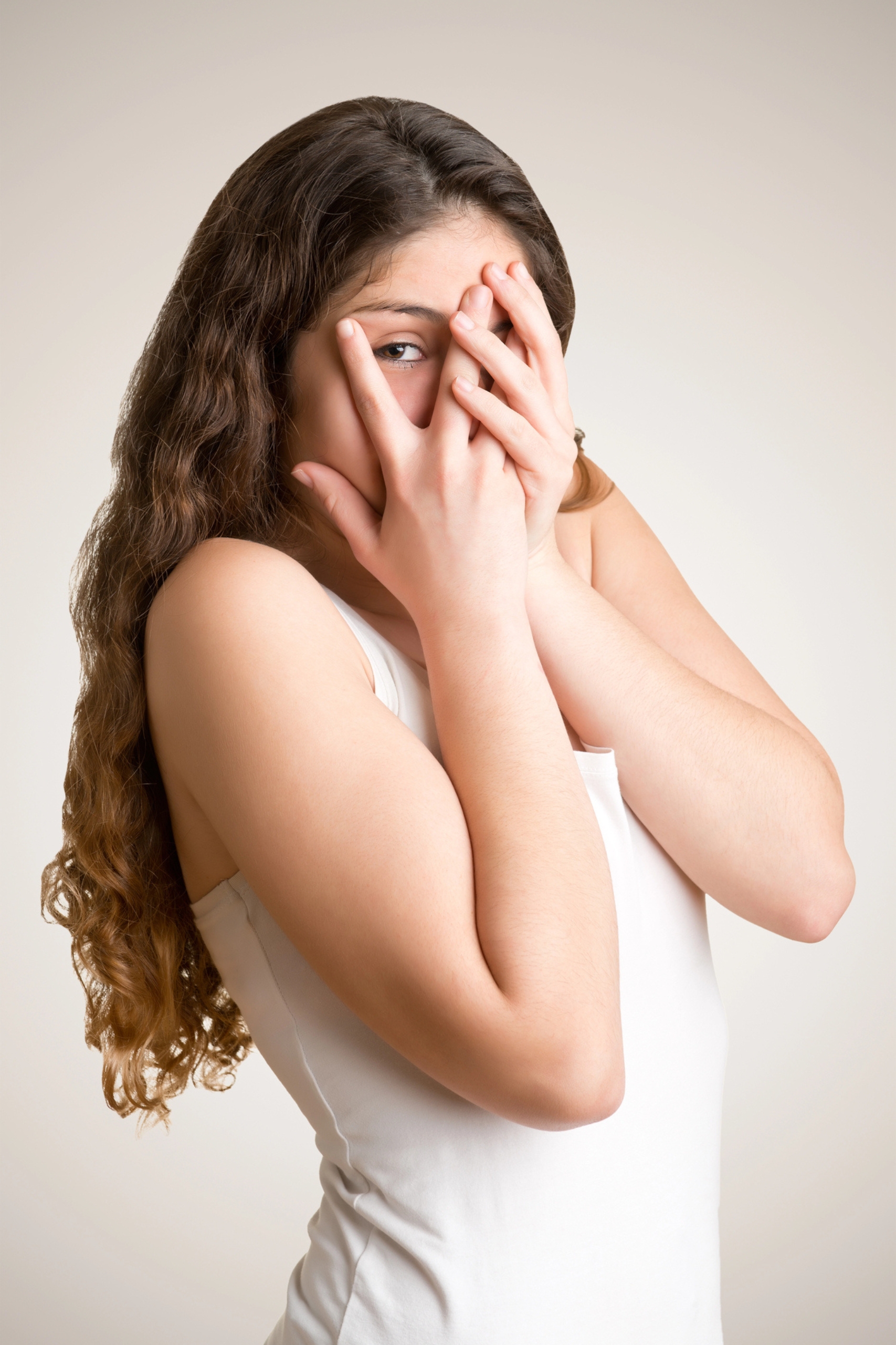 Woman with brown hair wearing a white dress with hands over her face in embarrassment.